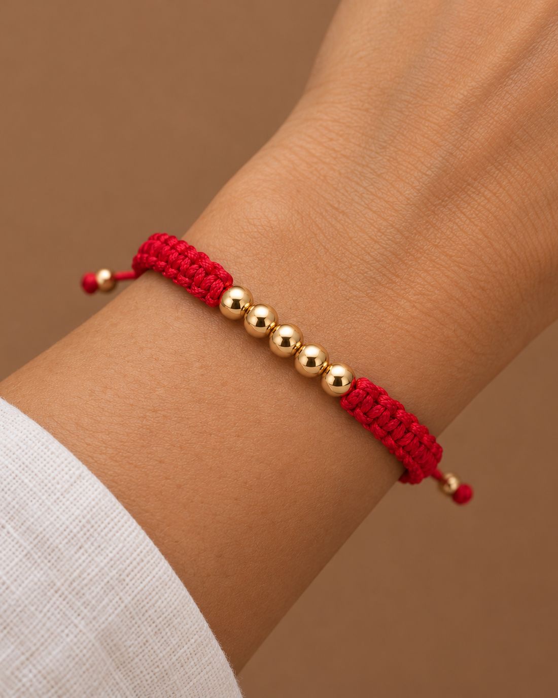 Pulsera tejida roja con cinco balines de oro, puesta en la muñeca