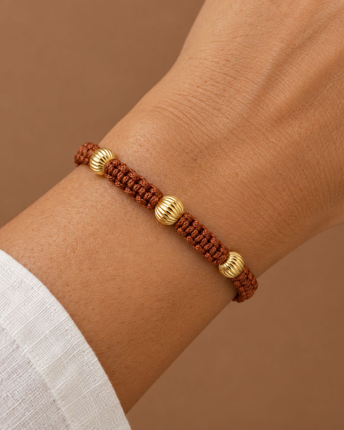 Pulsera tejida café con oro corrugado, puesta en la muñeca