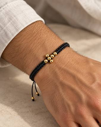 Pulsera tejida negra con cruz de balines de oro, puesta